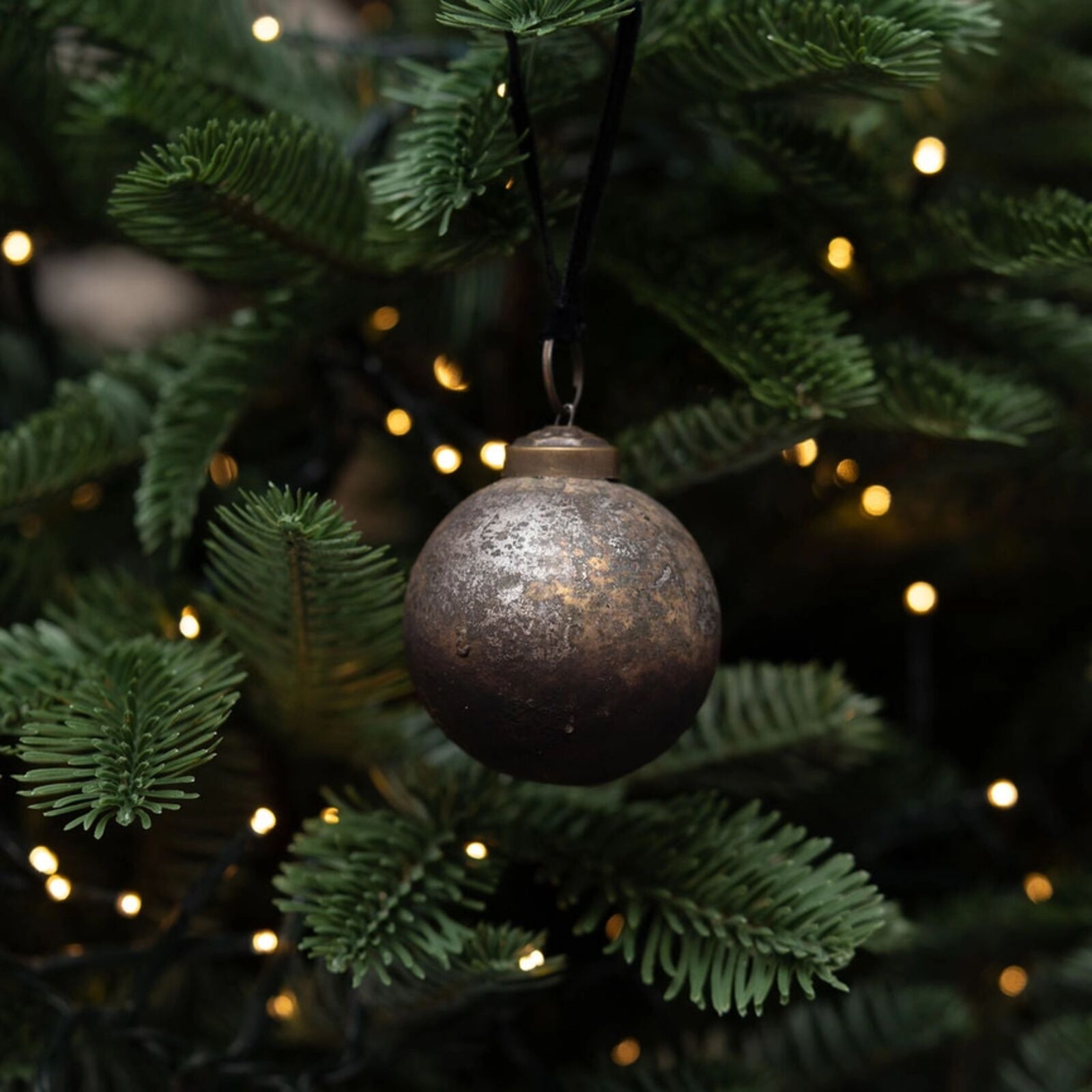 Decorative ornament hanging on a Christmas tree with lights in the background