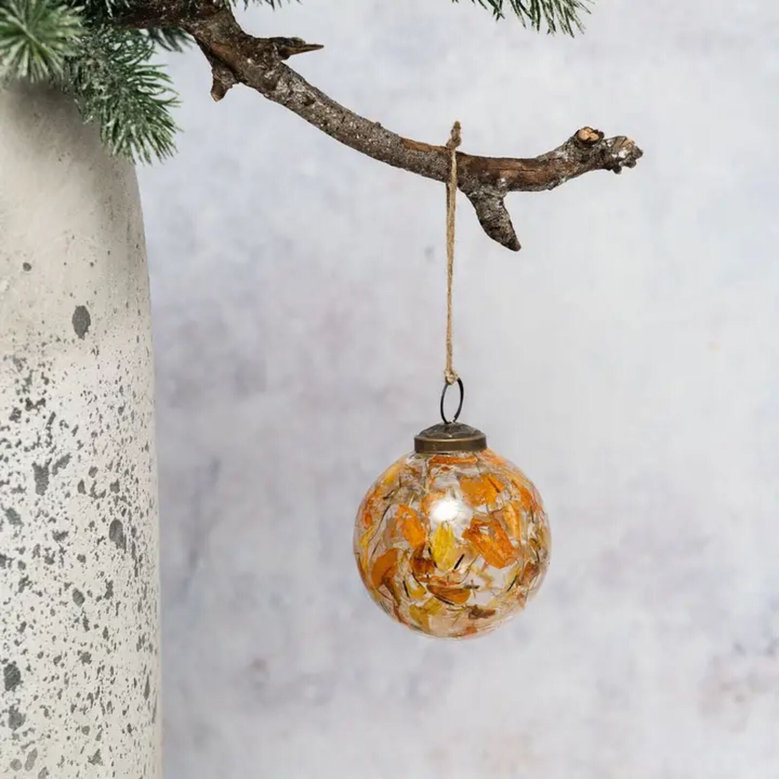 Decorative glass ornament with orange speckles hanging from a branch against a light background