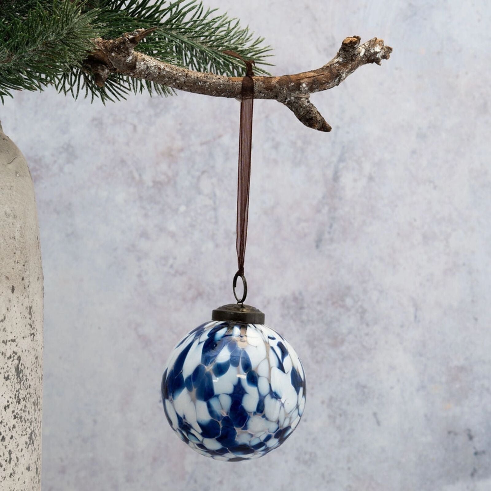 Decorative blue and white speckled ornament hanging from a branch against a light gray background.