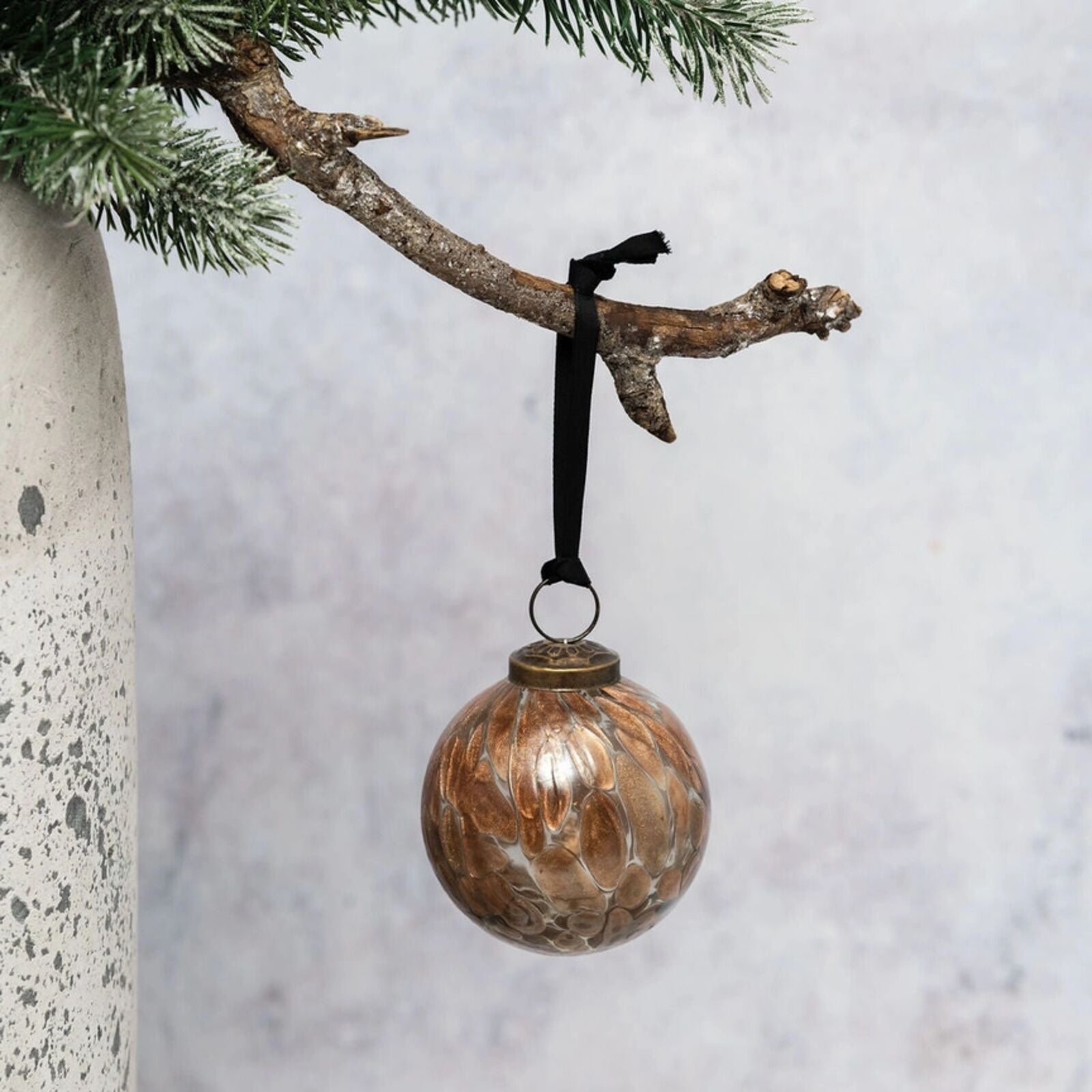 Decorative glass ornament hanging on a branch with a snowy background