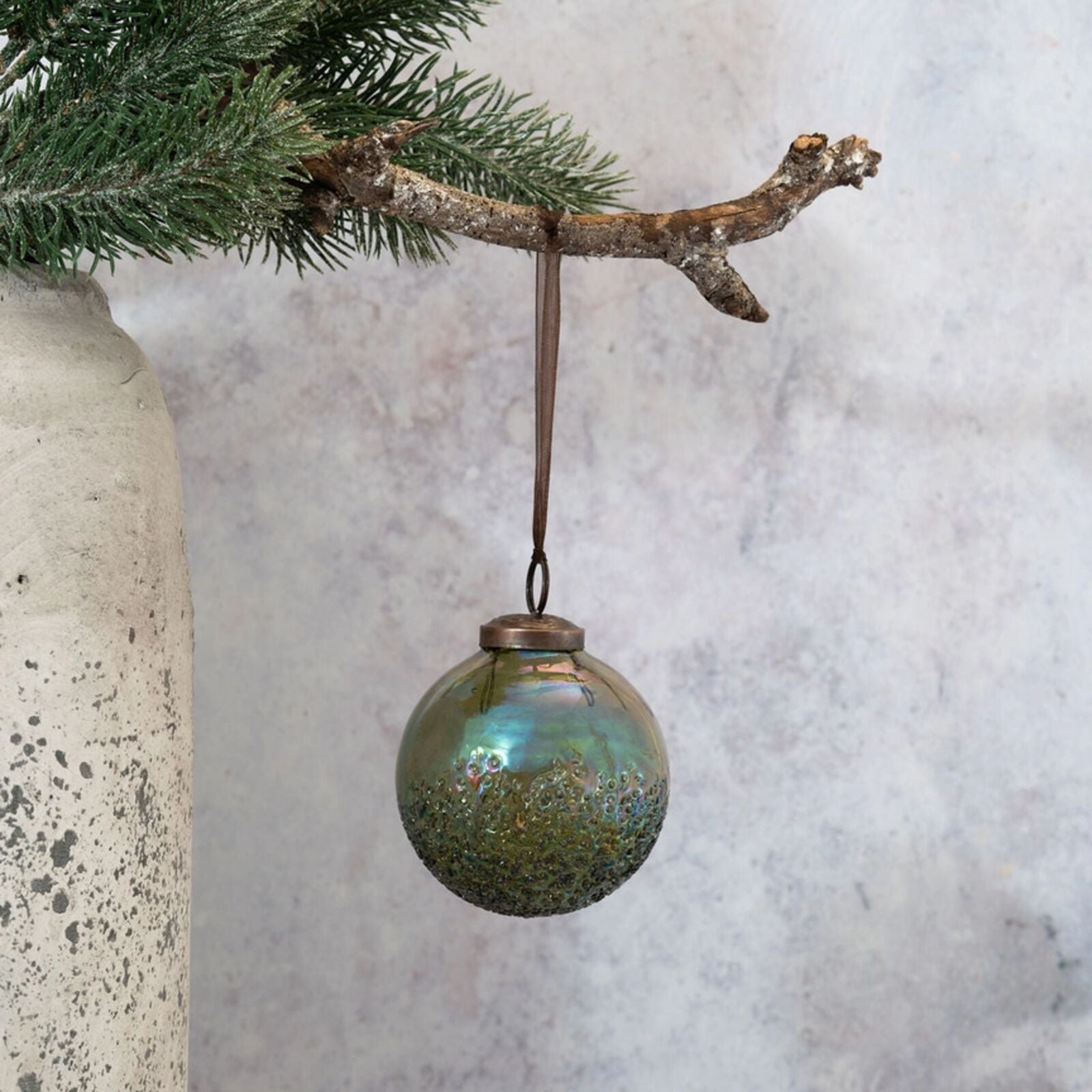 Decorative glass ornament hanging from a branch against a textured wall.