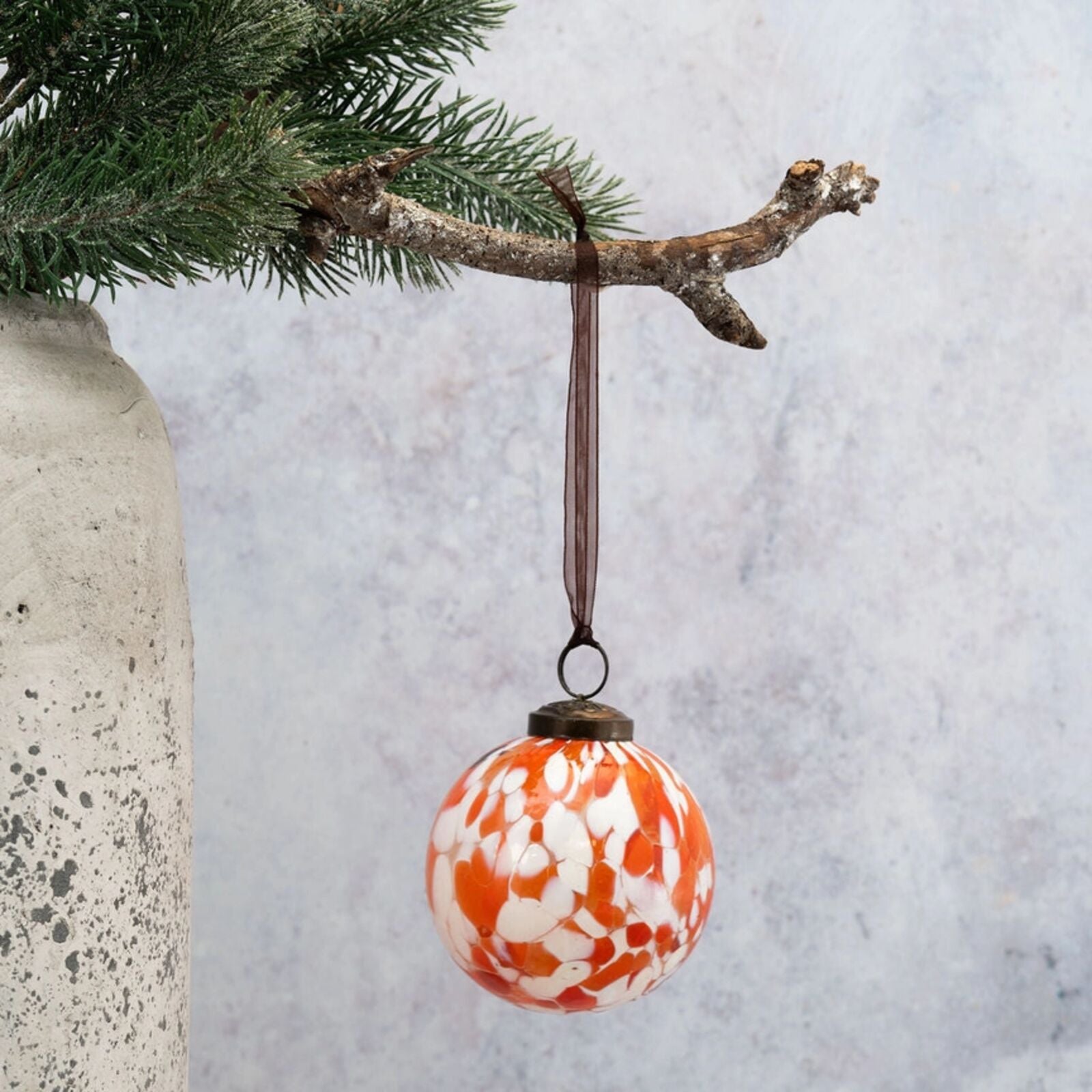 Decorative orange and white ball ornament hanging from a branch against a light gray background.