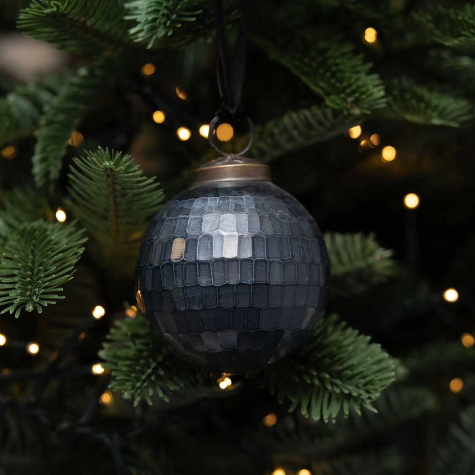 Black disco ball ornament on a Christmas tree with blurred lights in the background