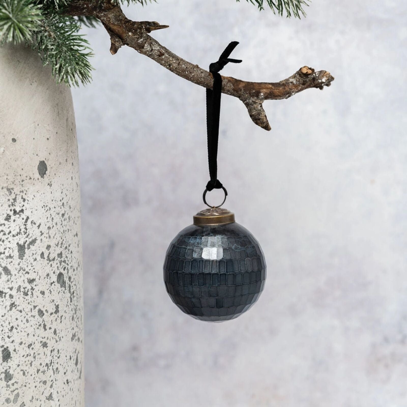 Black textured Christmas ornament hanging from a branch against a light background