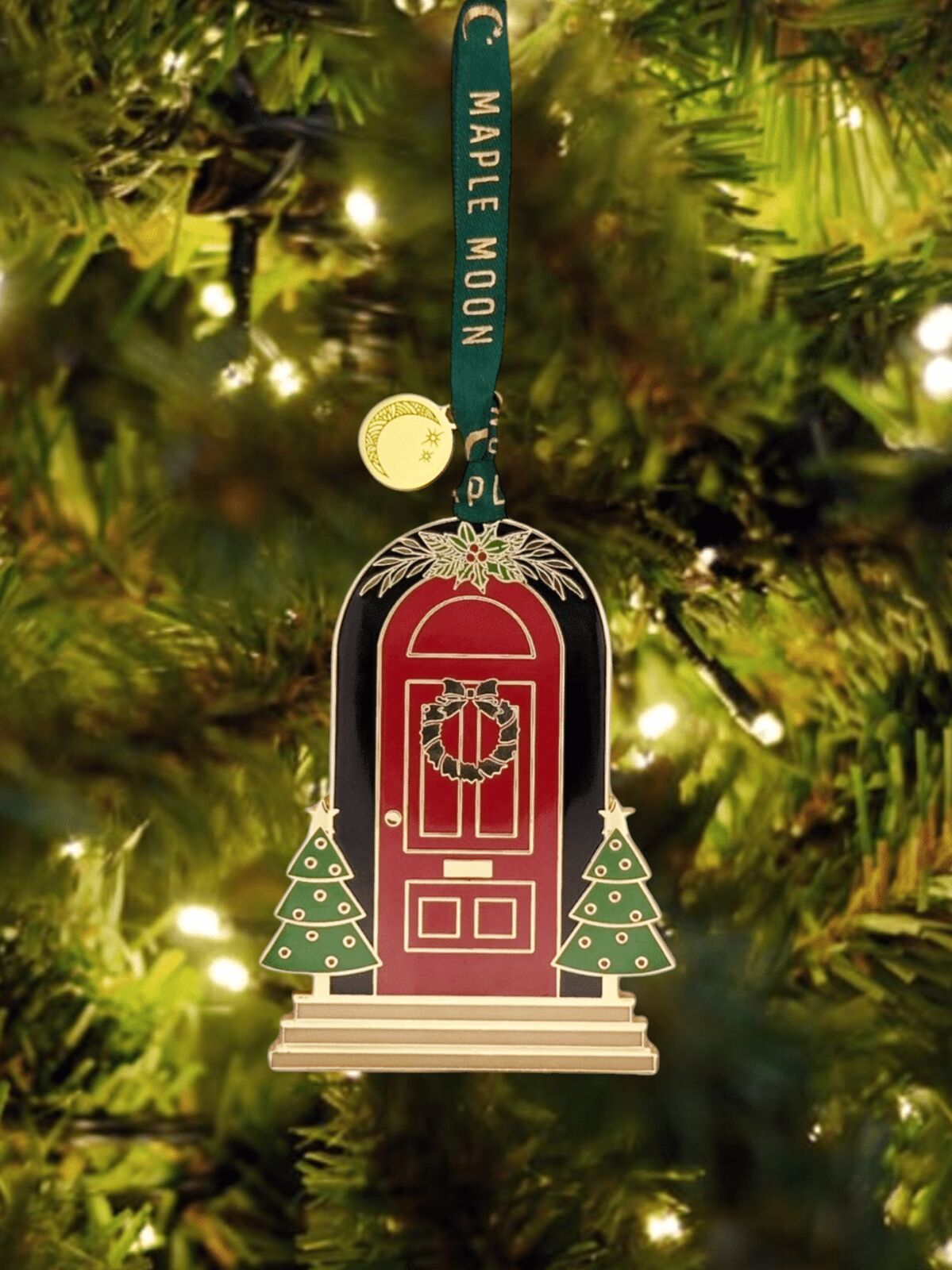 Decorative Christmas ornament of a red door with wreath, trees, and steps on a green tree.