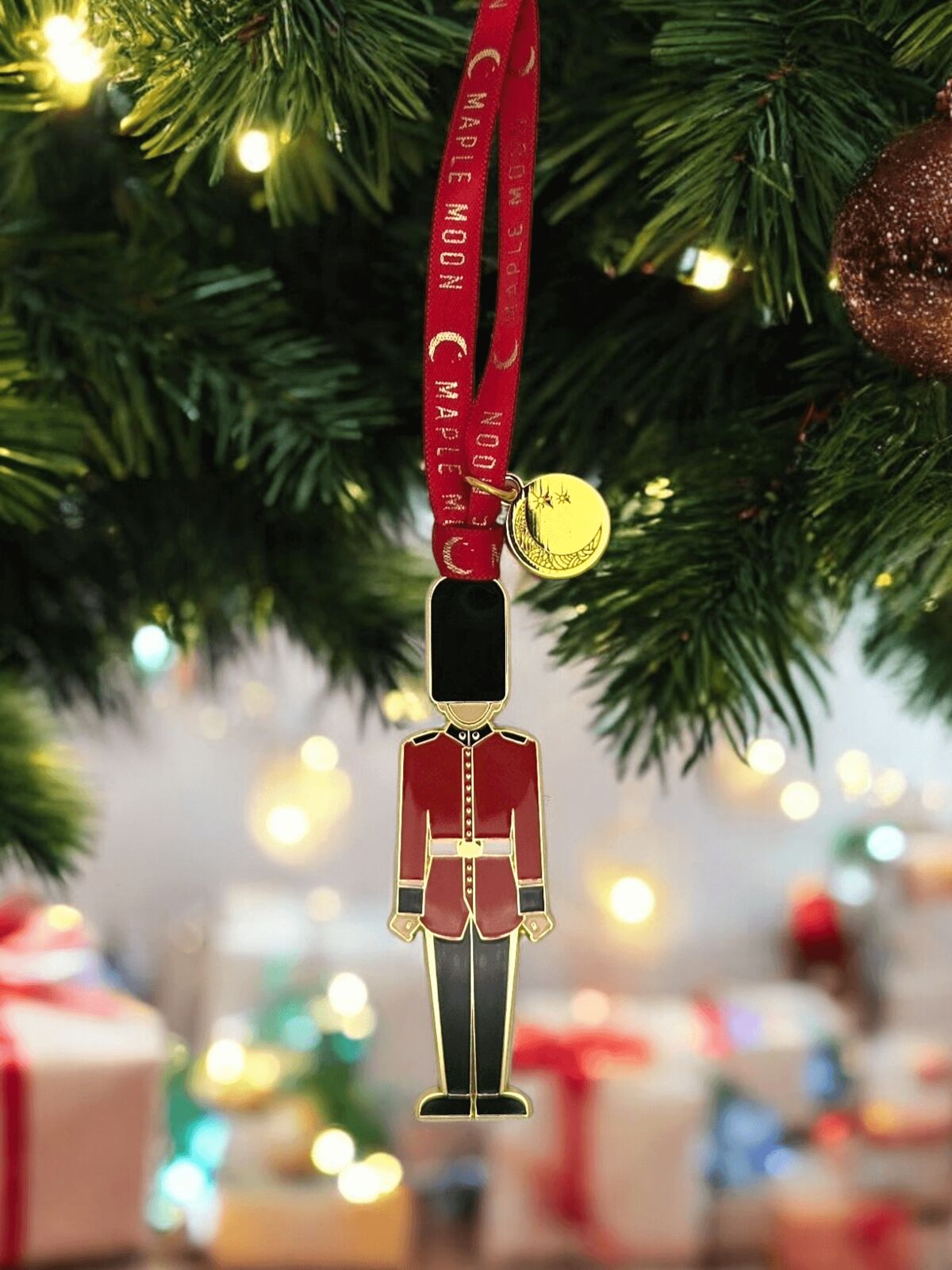 Decorative ornament resembling a toy soldier with a gold badge on a red lanyard, hanging on a Christmas tree.