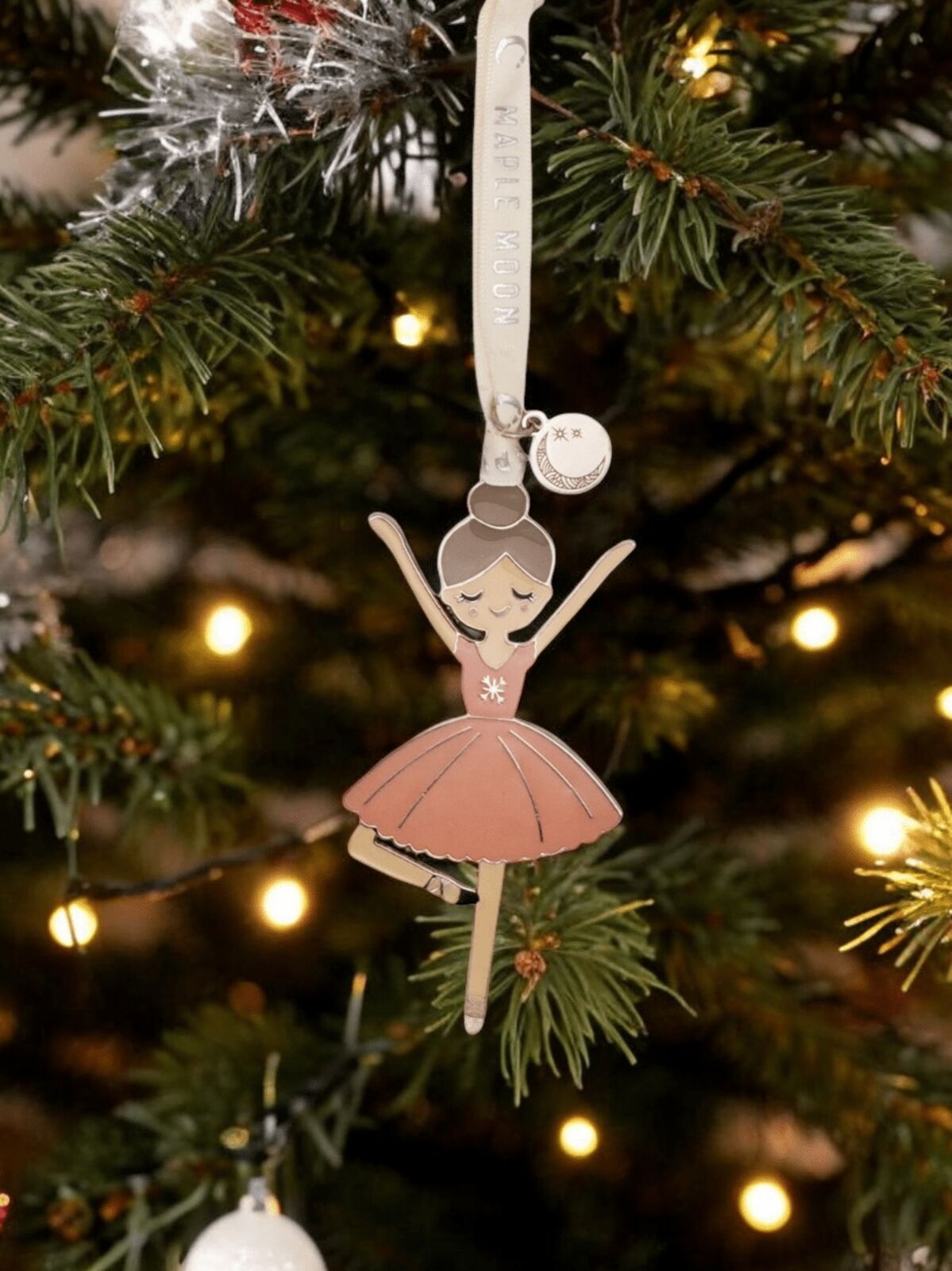 Decorative ornament of a ballerina on a Christmas tree with lights in the background