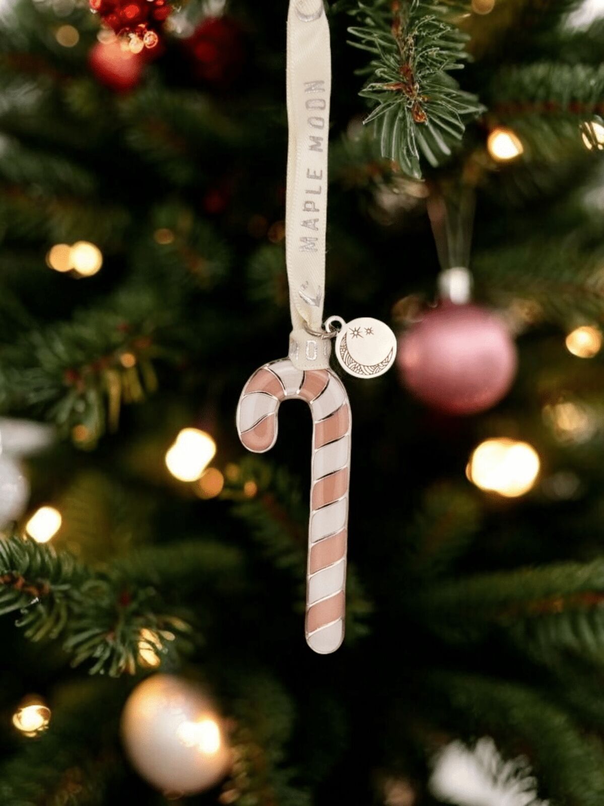 Candy cane ornament with 'Maple Moon' text hanging on a Christmas tree.