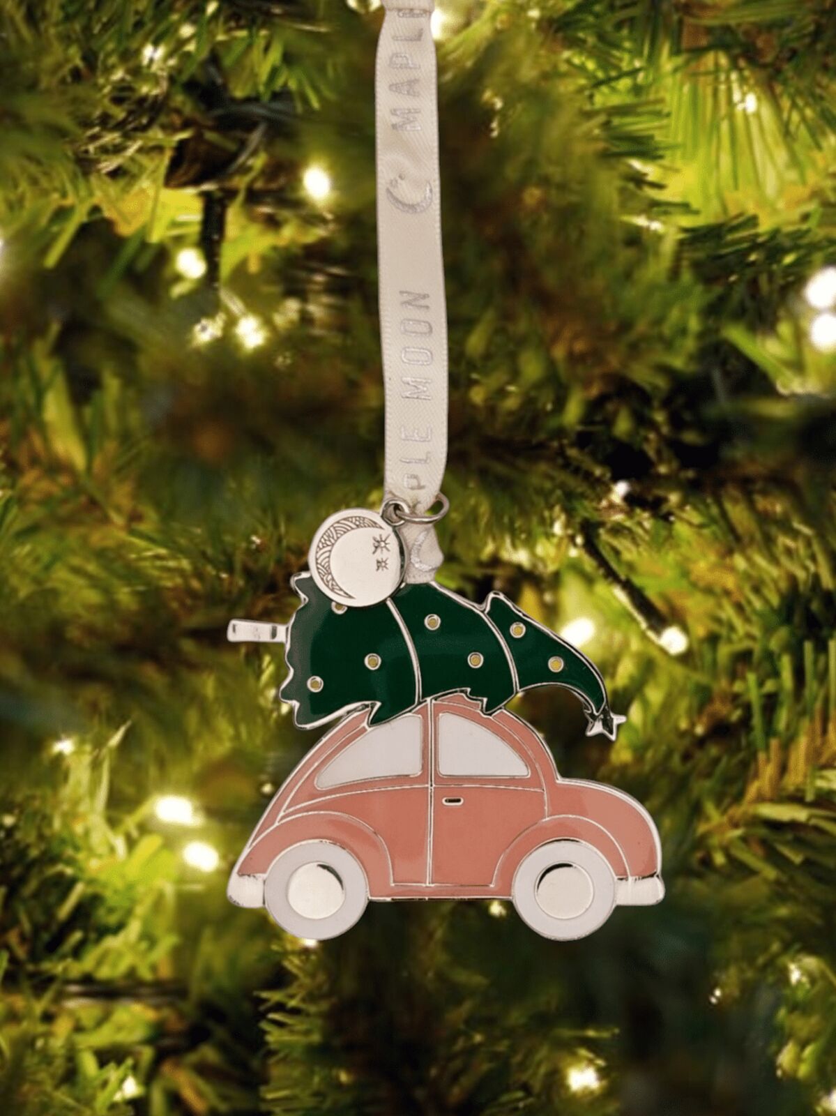 Decorative ornament of a pink car with a green tree on top, hanging from a ribbon on a Christmas tree.