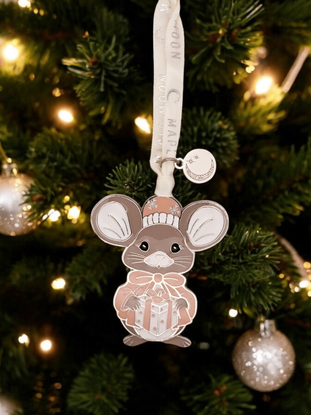Decorative mouse ornament on a Christmas tree with lights in the background