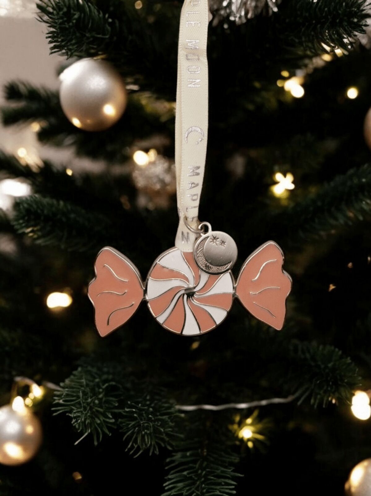 Decorative ornament shaped like a sweet with pink wrapper hanging on a Christmas tree.