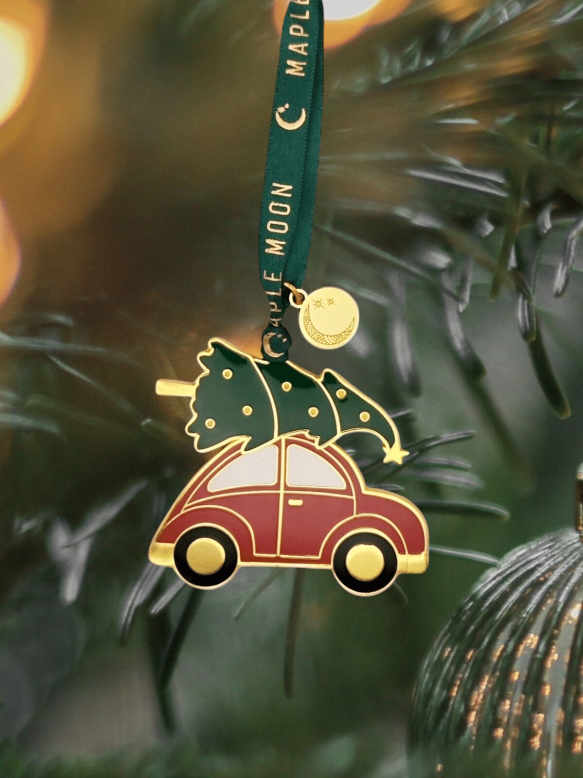 Decorative ornament with a car carrying a Christmas tree, hanging on a tree branch.