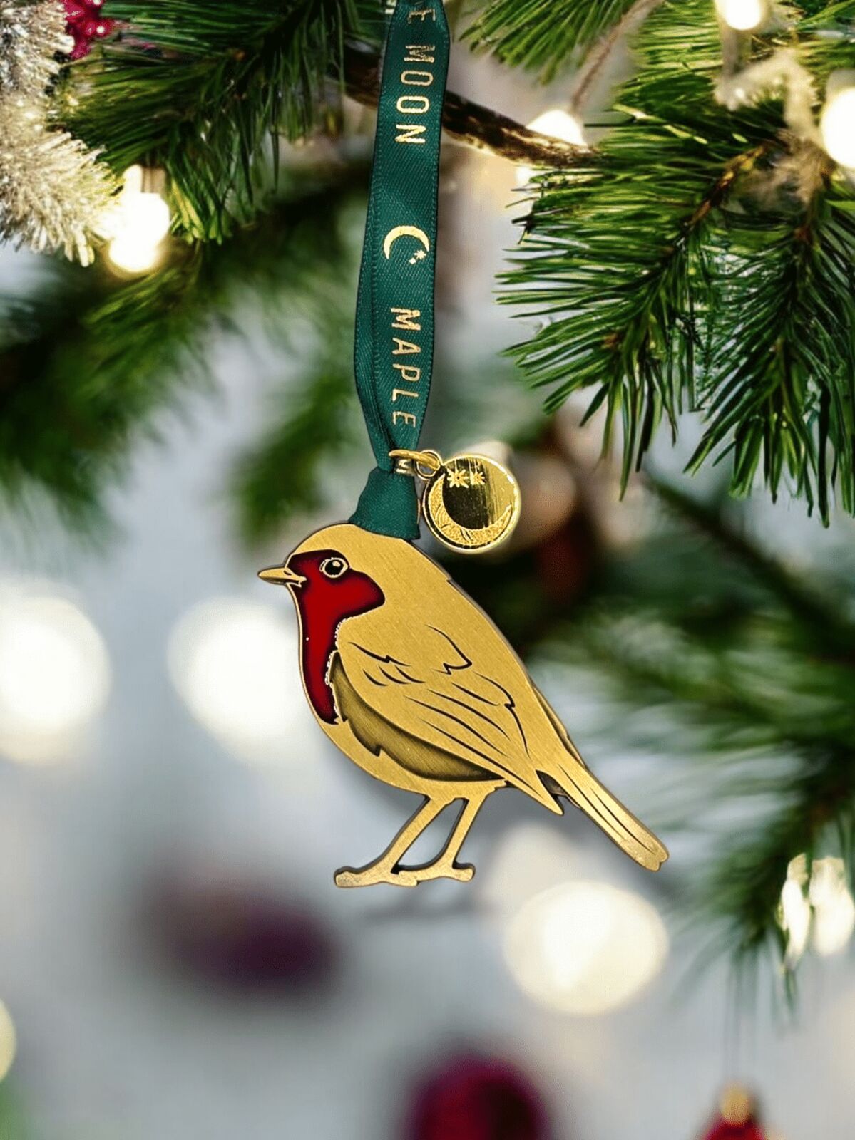Decorative bird ornament on a green ribbon with 'C. Maple' text, hanging on a Christmas tree.