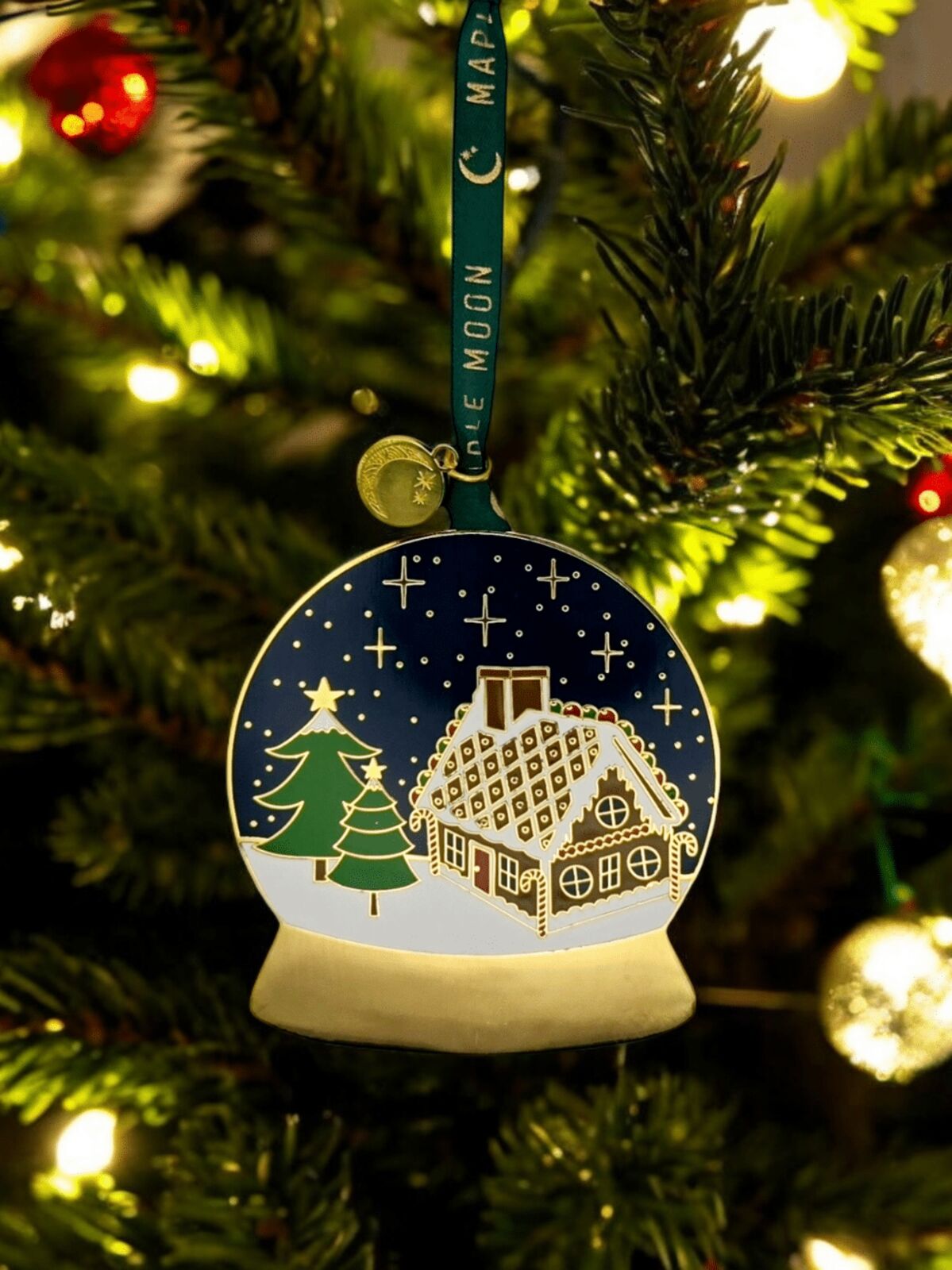 Christmas ornament with a house and tree design on a decorated tree.