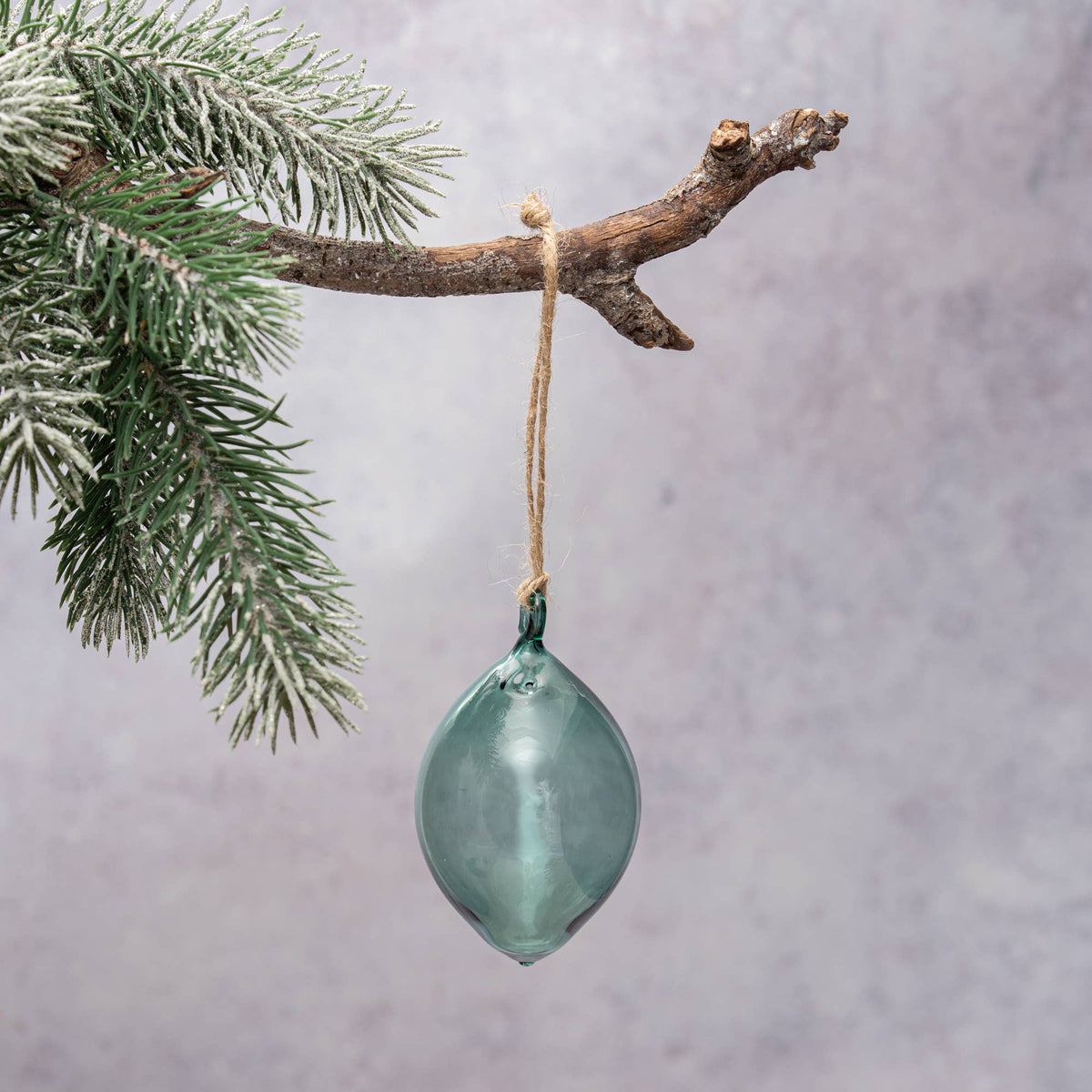 Green glass ornament hanging from a branch with a gray background