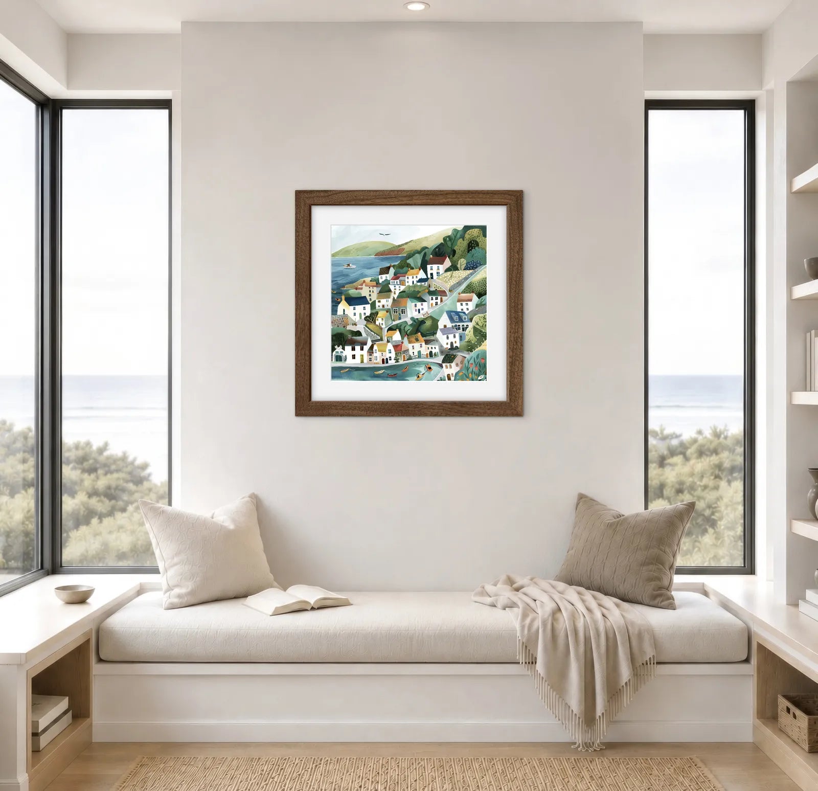 Framed artwork of a coastal scene on a wall above a window seat with pillows and a blanket.
