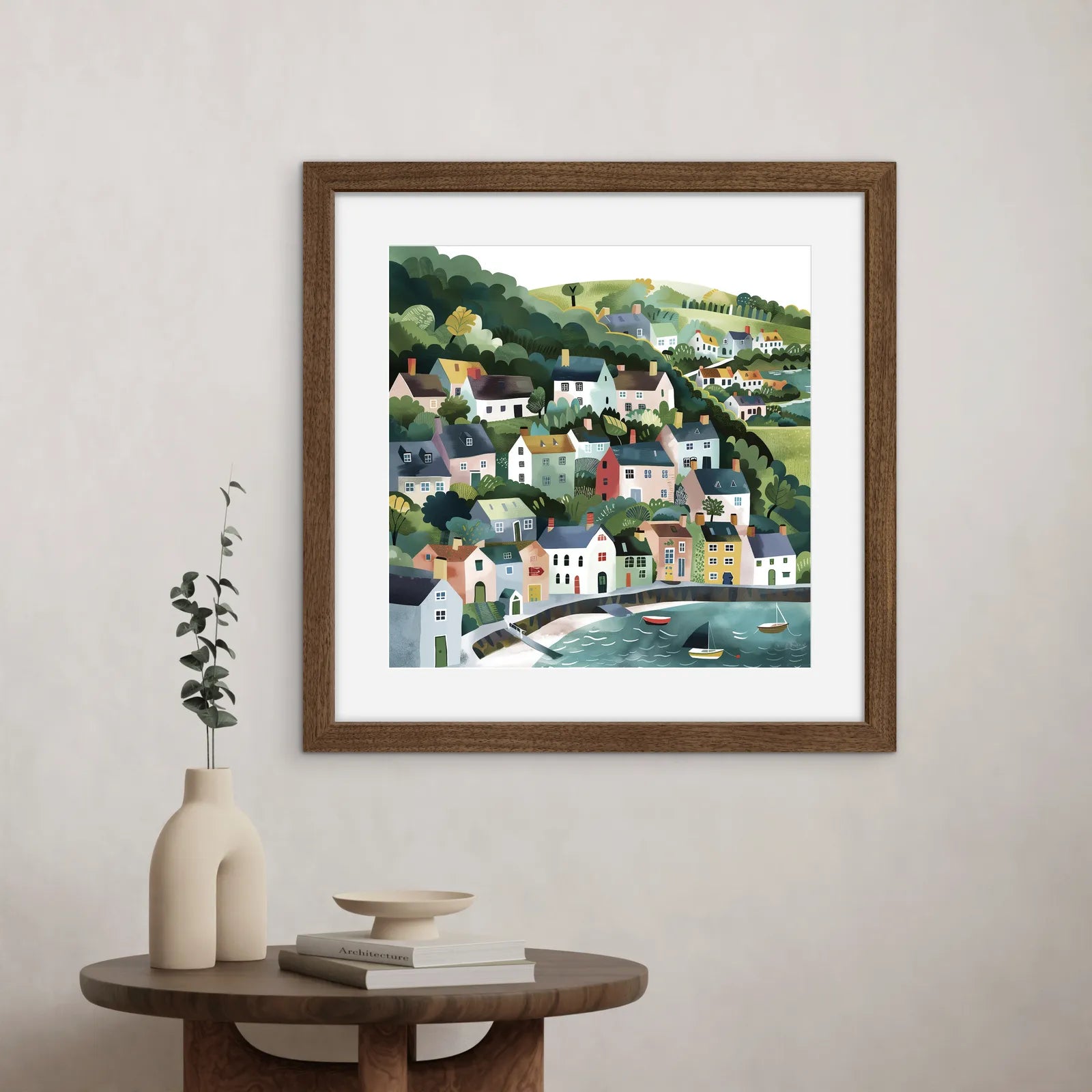 Framed artwork of a village by a lake on a wall above a table with decor items.