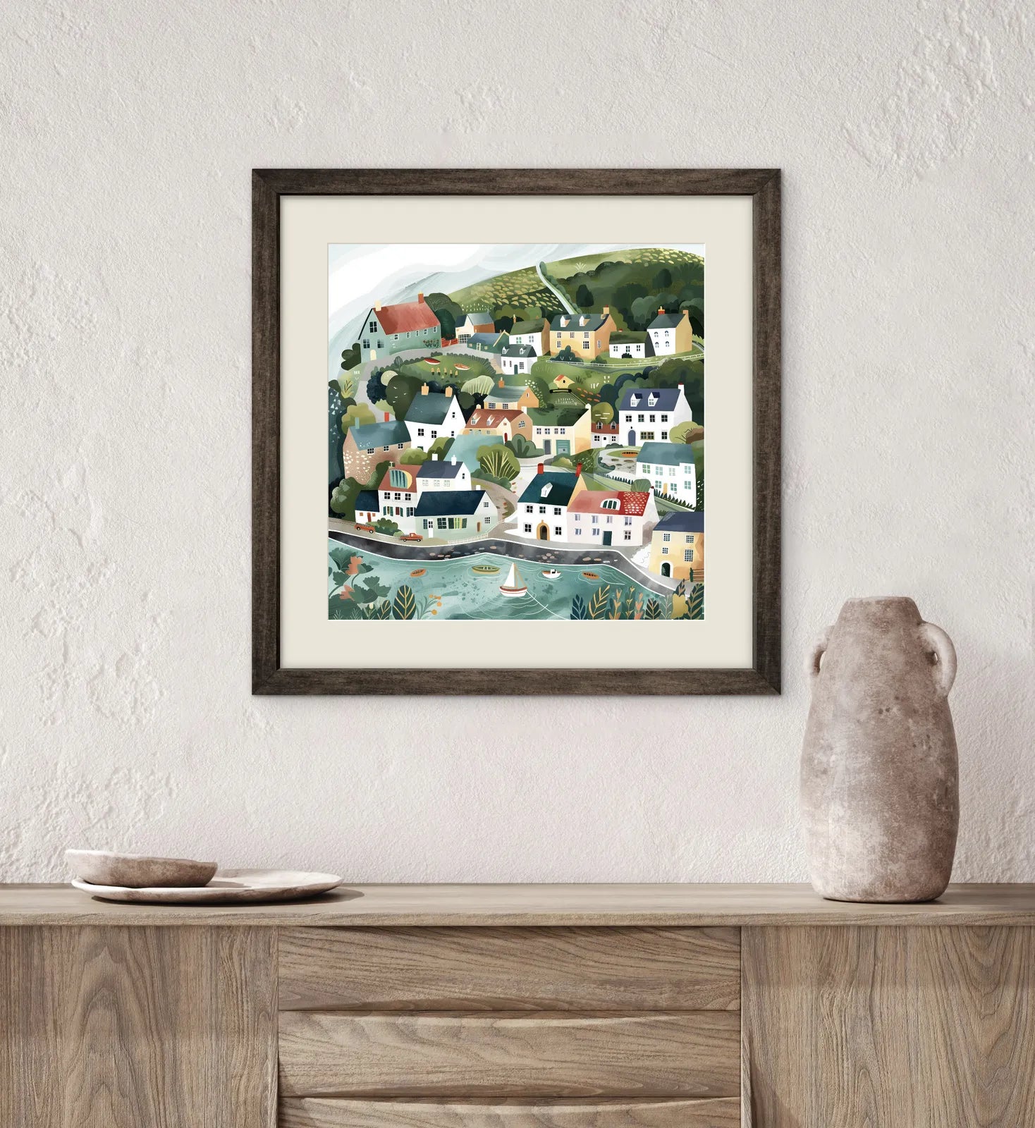 Framed artwork of a coastal village scene on a wall above a wooden cabinet.