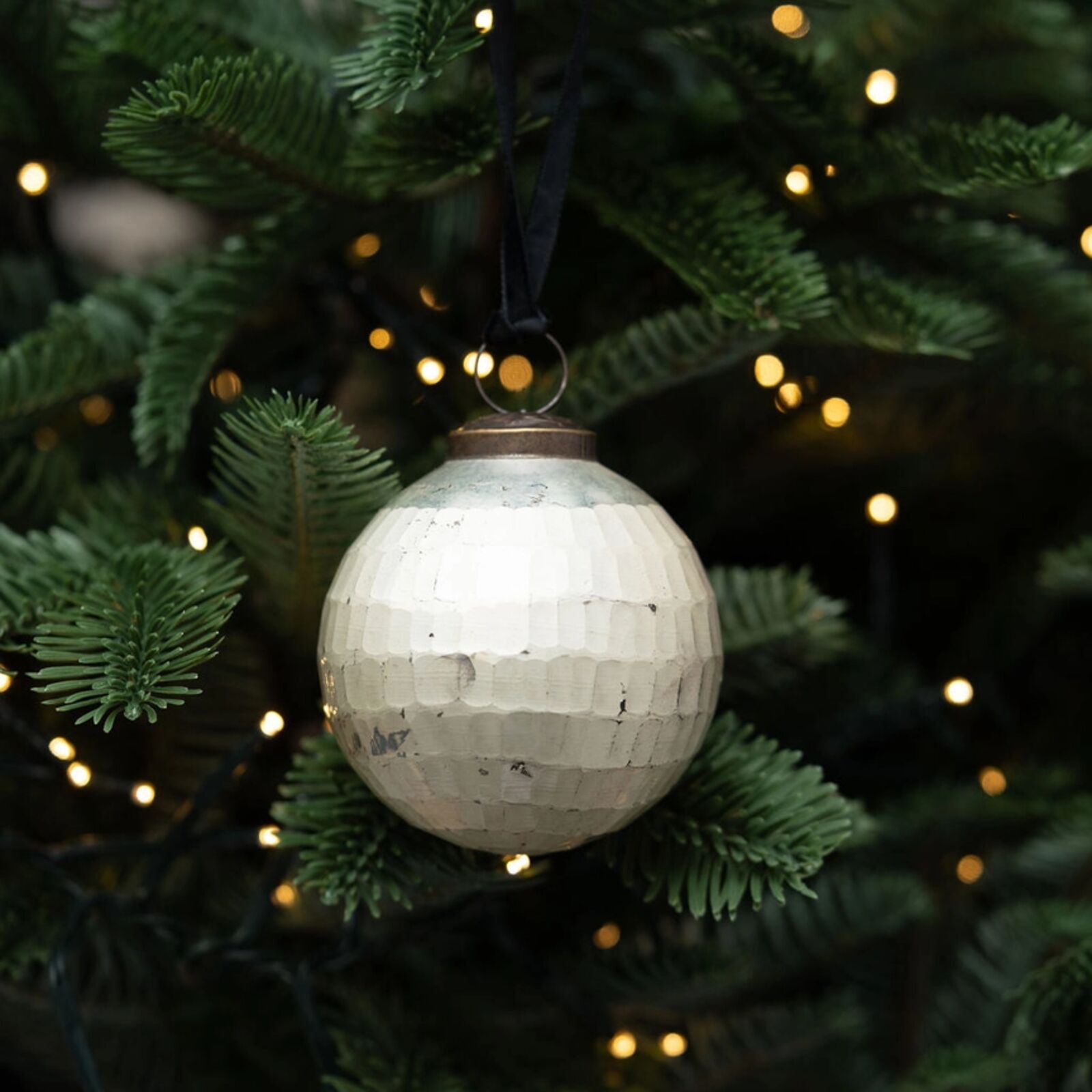 Decorative disco ball ornament on a Christmas tree with lights in the background