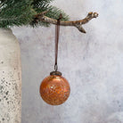 Bronze ornament hanging from a branch with a textured vase and light gray background