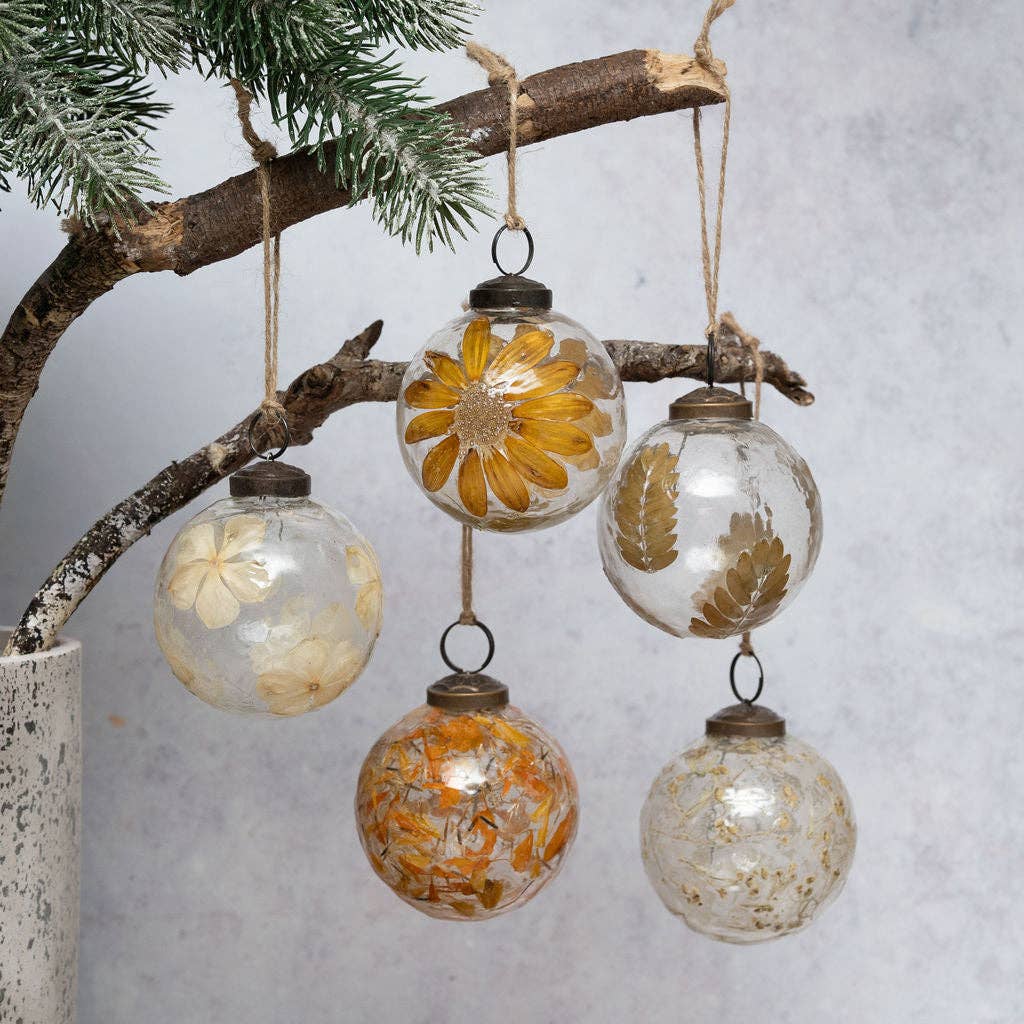 Five clear glass hanging ornaments decorated with dried flowers and leaves, suspended from a rustic tree branch against a soft light gray background.