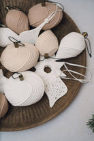 A collection of seashell-shaped Christmas ornaments in natural beige and white, arranged on a round wooden tray.