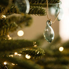 A clear glass teardrop ornament hanging from a jute string on a decorated Christmas tree with warm bokeh lights.