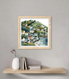 Framed artwork of a coastal village scene on a wall above a shelf with decor items.